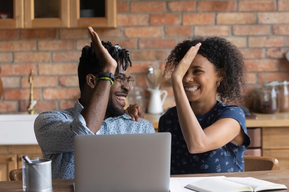 African-American couple giving high-fives to each other behind a computer 