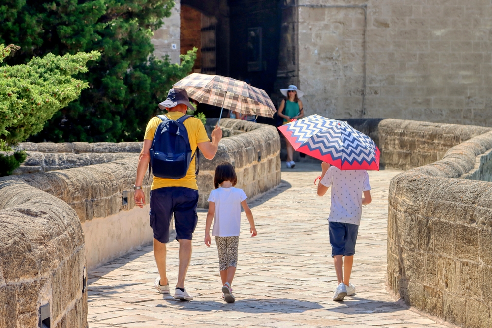 Man with 2 kids walking under parasols and umbrellas