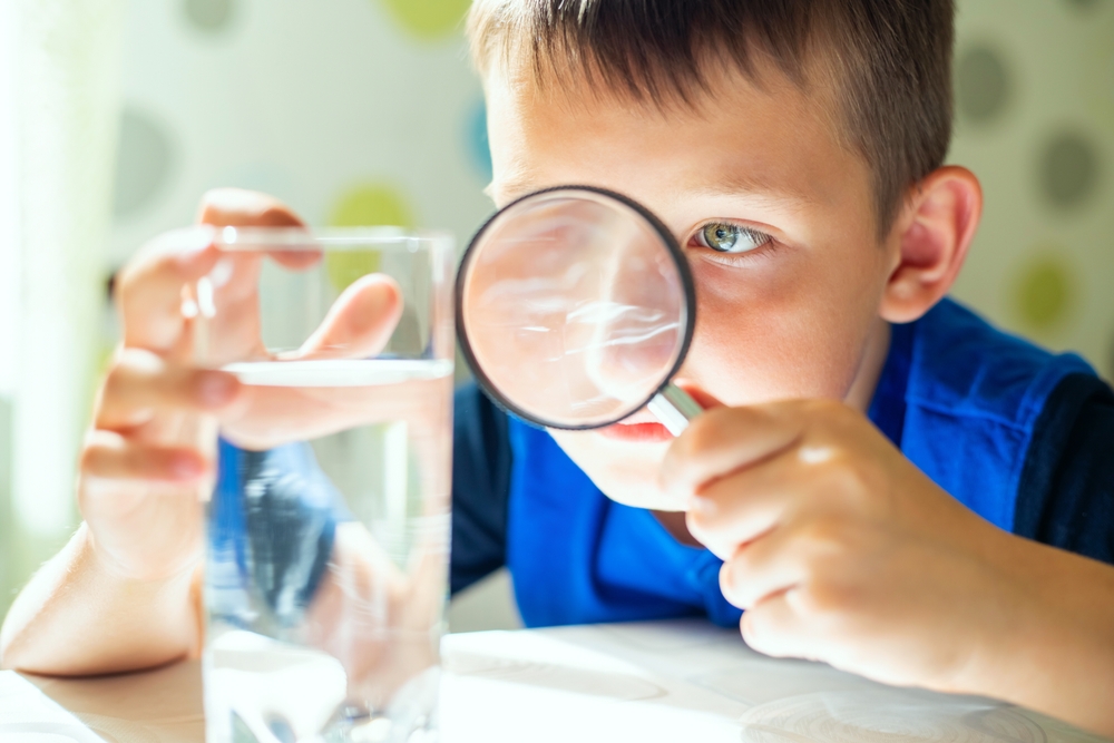 boy with magnifying glass examining glass of tap water