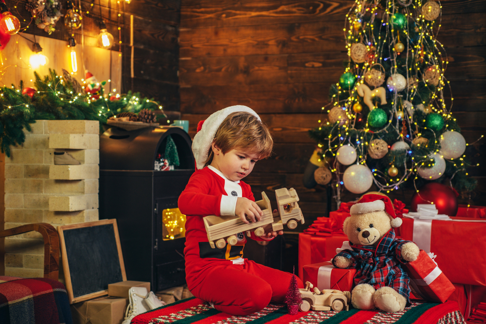 boy in santa pajamas opening favorite toys under a Christmas tree