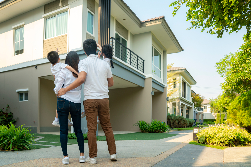 Couple, each holding a young child, look at their home and wonder about insurance