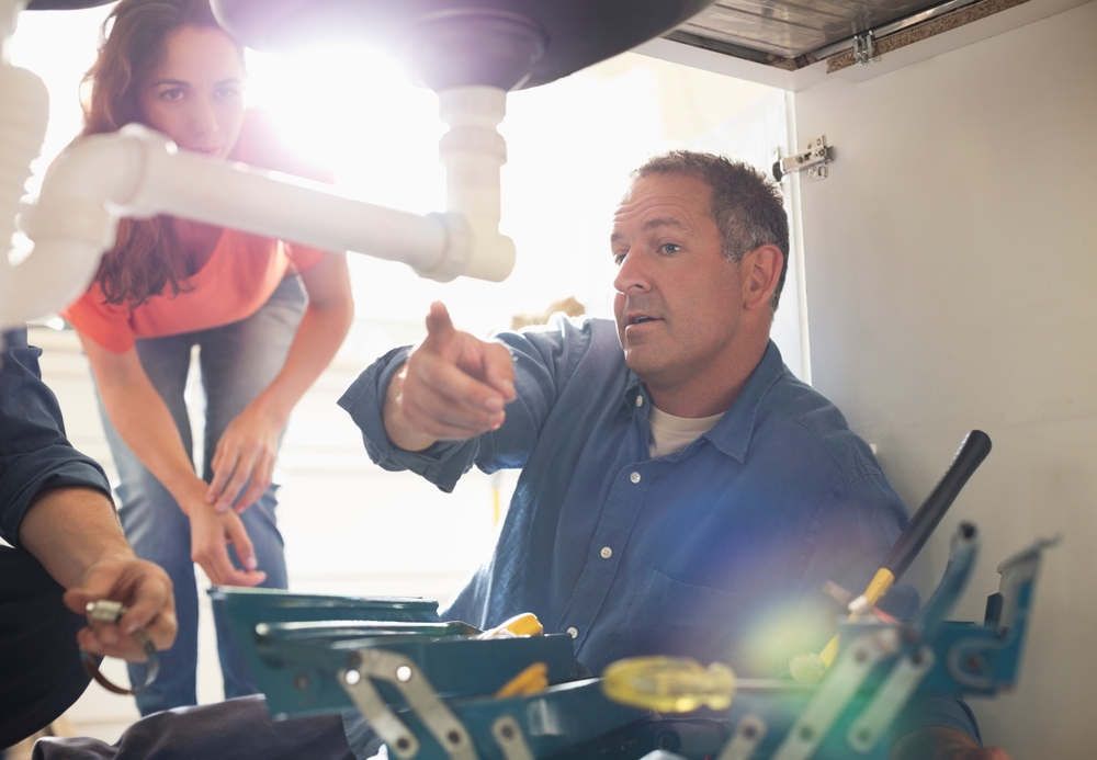 plumber under sink showing customer a problem